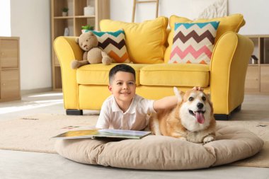 Little happy Asian boy reading book with cute Corgi dog at home