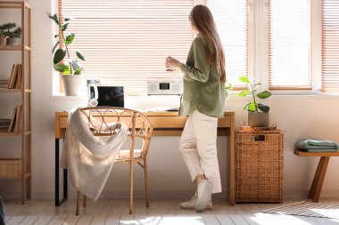 Genç bir kadın şık bir ofiste işyerinin yakınında kahve içiyor.