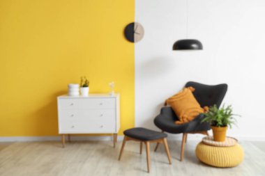 Şık oturma odasının içinde siyah koltuk, çekmeceler, sarı duvarda lamba ve saat, bulanık görüş.