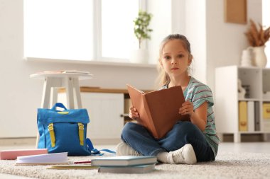 Kitapları ve sırt çantasıyla evde oturup ders çalışan sevimli küçük kız.