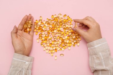 Pembe arka planda balık yağı haplı kadın eller.