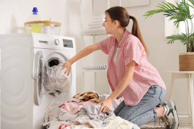 Kirli çamaşırları evdeki çamaşır makinesine koyan genç bir kadın.