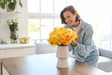 Mutfaktaki masasında nergis olan genç bir kadın.