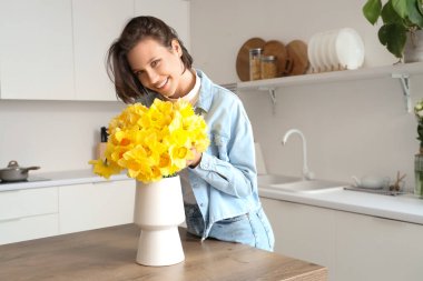 Mutfaktaki masasında nergis olan genç bir kadın.