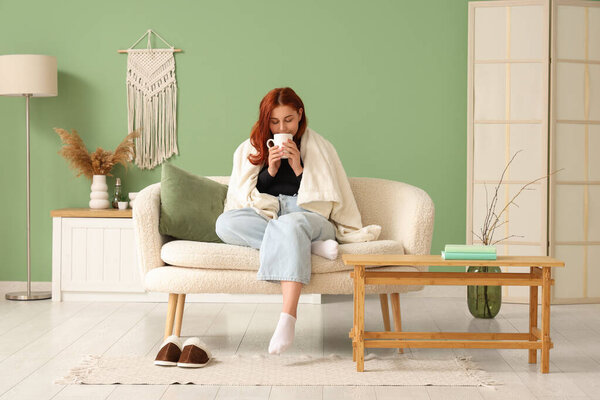 Молодая женщина с теплым клетчатым чаем пьет чай на диване дома
