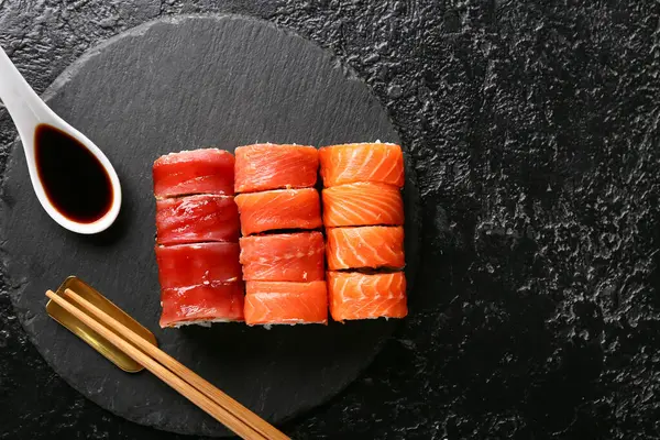 Lezzetli suşi ruloları ve çubuklar, soya soslu yemek çubukları ve siyah grunge arka plan.