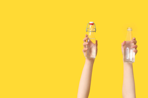 Female hands with bottles of water on yellow background, closeup