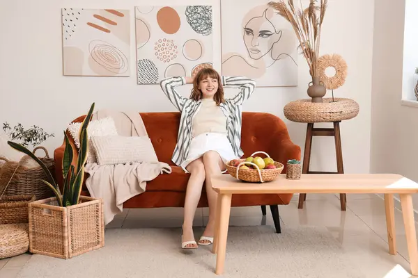 Beyaz oturma odasındaki kahverengi kanepede dinlenen genç ve güzel bir kadın.