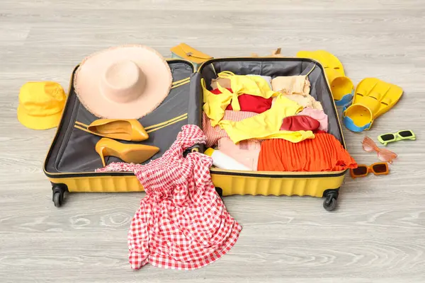 İçinde kadın kıyafetleri, güneş kremi ve yüzgeçler olan açık bir bavul. Seyahat kavramı