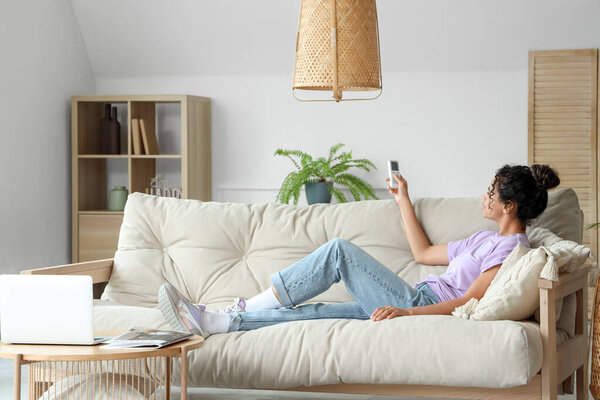 Young African-American woman turning on air conditioner at home
