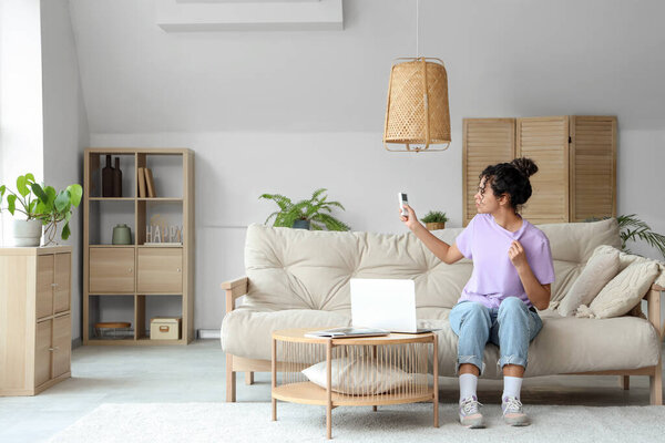 Young African-American woman turning on air conditioner at home