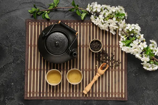 Bardaklı çaydanlık, bir kaşık kuru çay ve siyah grunge arka planda çiçekler.