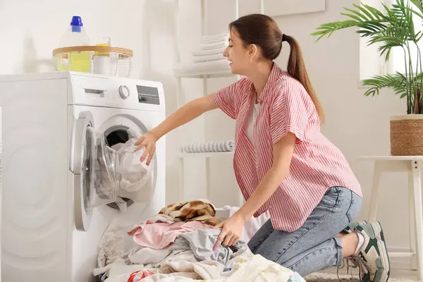 Kirli çamaşırları evdeki çamaşır makinesine koyan genç bir kadın.