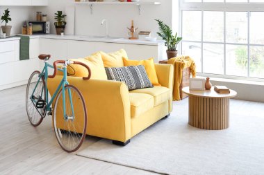 İçinde sarı kanepe, sehpa, tezgah ve bisiklet olan oturma odası.