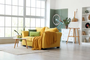 Sarı kanepeli, sehpalı, çiçekli ve bisikletli şık bir oturma odası.