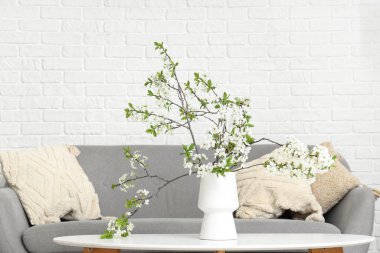 Oturma odasındaki kanepenin yanındaki sehpanın üzerinde çiçek açan bir vazo.