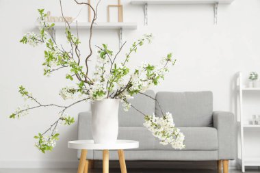 Beyaz oturma odasındaki yumuşak kanepenin yanındaki sehpanın üzerinde çiçek açan bir vazo.