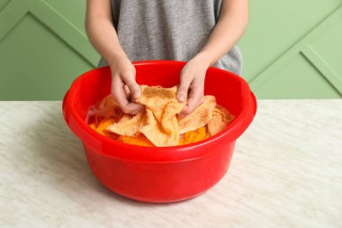 Kadın yeşil arka planda plastik bir leğende çamaşır yıkıyor.