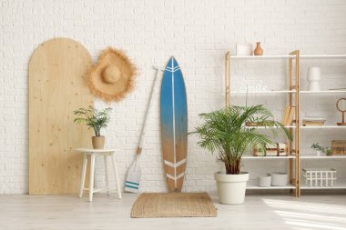 Beyaz tuğla duvarın yanında sörf tahtası ve raf ünitesi olan modern tarz bir oda.