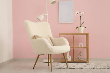 Pembe duvarın yanında beyaz koltuk, lamba ve raf ünitesi