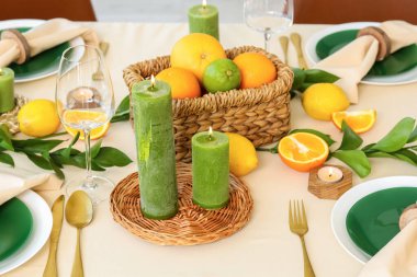 Oturma odasında turunçgil meyveleri, yanan mumlar ve beyaz masa örtüsü olan güzel bir masa.