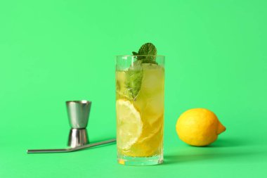 Limonlu bir bardak lezzetli limonata, yeşil arka planda ölçü kabı ve saman.