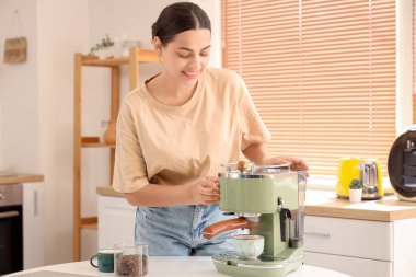 Mutfakta modern kahve makinesi olan güzel, genç ve mutlu bir kadın.