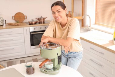 Mutfakta modern kahve makinesi olan güzel, genç ve mutlu bir kadın.