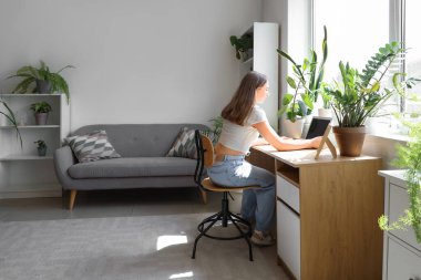 Young woman working with laptop at table near window in office