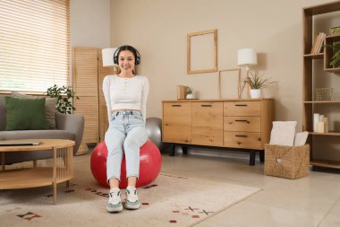 Kulaklıklı genç Asyalı kadın evde spor salonunda oturuyor.