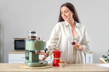 Evinde bir fincan sıcak espresso ve kahve makinesi olan güzel bir kadın.