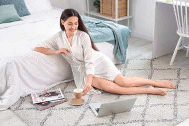 Evinde bir fincan sıcak kahve ve dizüstü bilgisayarı olan güzel bir kadın.