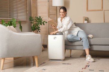 Genç kadın kanepede oturuyor ve oturma odasındaki modern nemlendiriciyi açıyor.