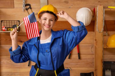 Atölyede ABD bayrağı taşıyan genç bir kadın marangoz. İşçi Bayramı kutlamaları