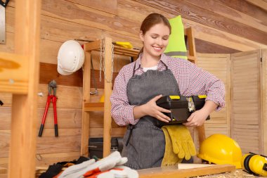 Atölyede alet çantası olan genç bir kadın marangoz. İşçi Bayramı kutlamaları