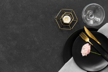 Siyah tabaklar, peçete, çatal bıçak, cam, mum ve çiçekli güzel bir masa.