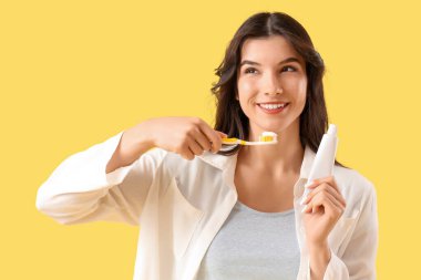 Sarı arka planda diş fırçası ve yapıştırmasıyla gülümseyen genç kadın, yakın plan.