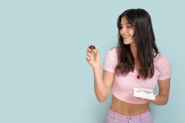 Mavi arka planda bir kutu çikolatalı şekerlemesi olan güzel genç bir kadın.