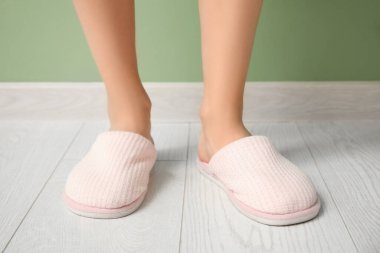 Yumuşak terlik giymiş bir kadının bacakları yeşil arka planda.