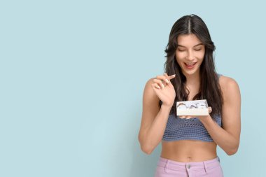 Mavi arka planda bir kutu lezzetli çikolata şekeri olan mutlu genç bir kadın.