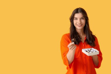 Sarı arka planda lezzetli çikolata şekerleri olan mutlu genç bir kadın.