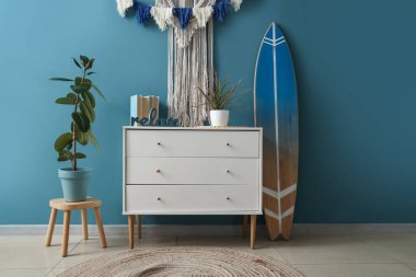 Interior of stylish room with tapestry, commode and surfboard