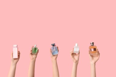 Pembe arka planda bir sürü parfüm şişesi olan kadın elleri.