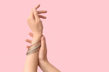Pembe arka planda güzel bilezikleri olan kadın elleri.