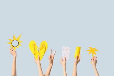 Mavi arka planda parmak arası terlik, bilet ve plaj aksesuarları olan eller.