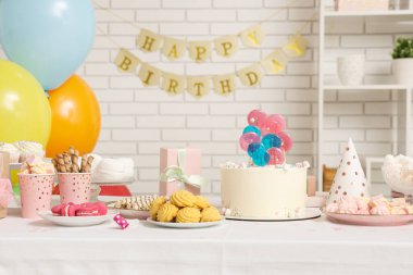 Beyaz tuğla duvara karşı doğum günü partisi için pasta, şeker ve dekor.