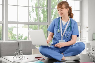 Klinikteki masada dizüstü bilgisayar kullanan bir kadın stajyer.