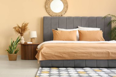 Rahat yatak, ayna ve vazo, güzel yatak odasındaki komodinin üzerinde otlar.