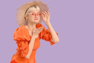 Güneş gözlüklü güzel bir genç kadının portresi eflatun arka planda öpüşüyor.