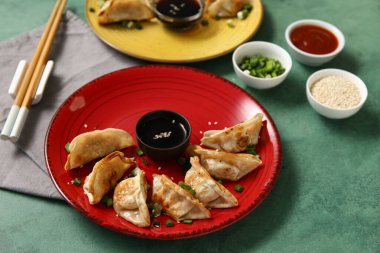 Kızarmış Japon gyoza tabağı ve yeşil arka planda bir kase soya sosu.
